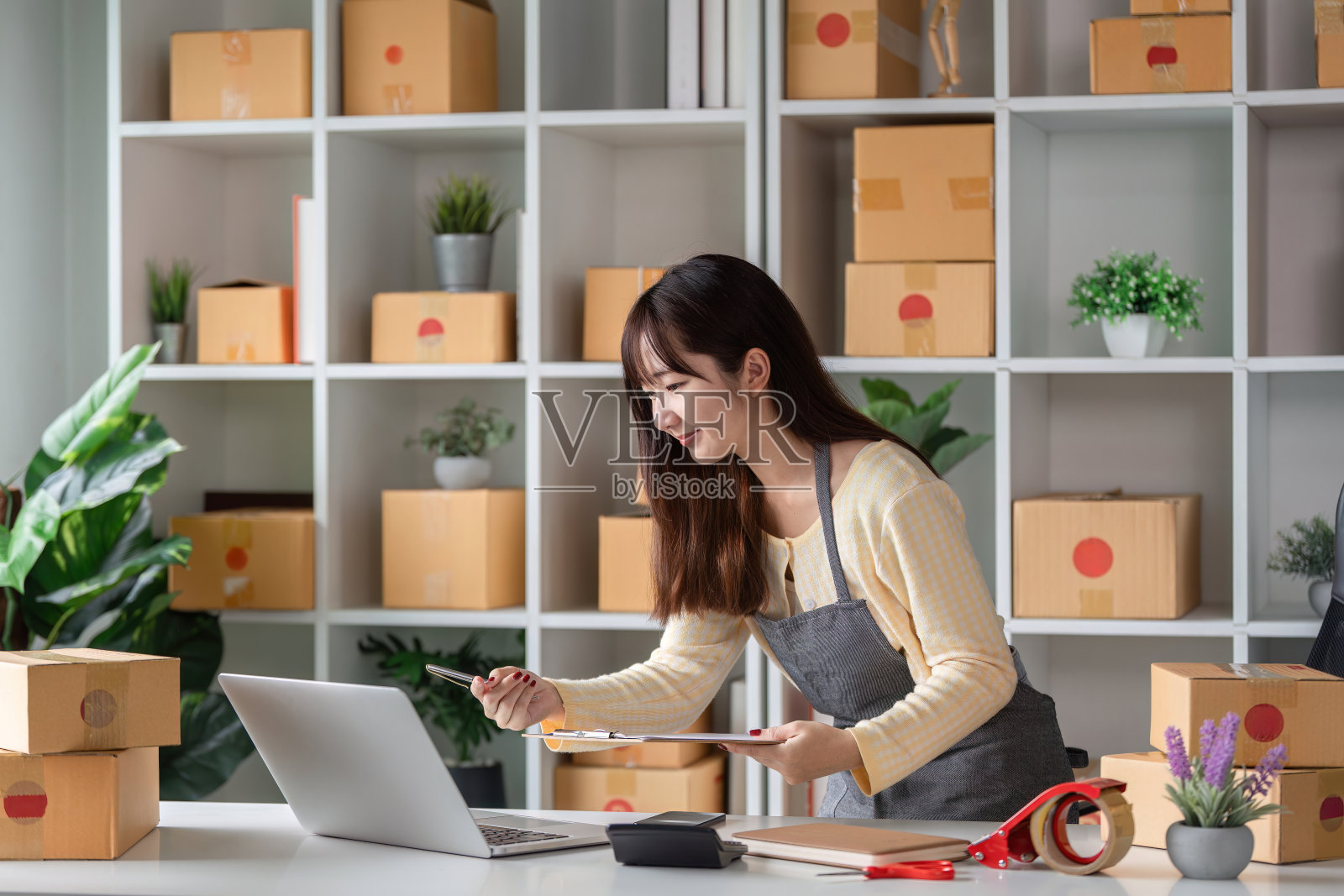 年轻女企业家在一个现代化的家庭办公室里用运输箱和笔记本电脑检查在线产品订单照片摄影图片