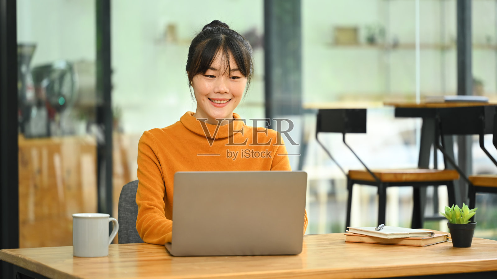 穿着黄色毛衣的年轻漂亮的亚洲女人在咖啡馆用笔记本电脑照片摄影图片