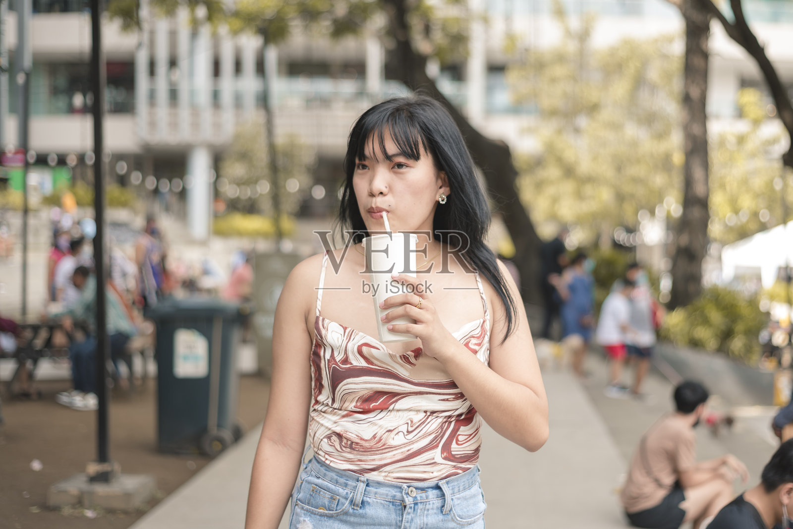 一名年轻女子路过一家购物中心的户外区域时，正在享用一杯冰凉的水果奶昔。照片摄影图片