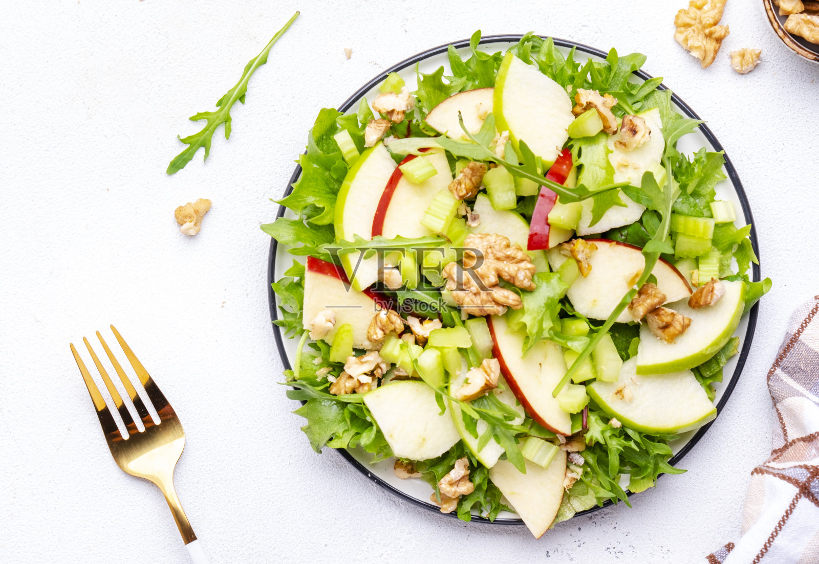 美味脆脆的素食沙拉，绿色和红色的苹果，新鲜的芹菜，生菜，芝麻菜和核桃在盘子里，白色背景，俯视图照片摄影图片