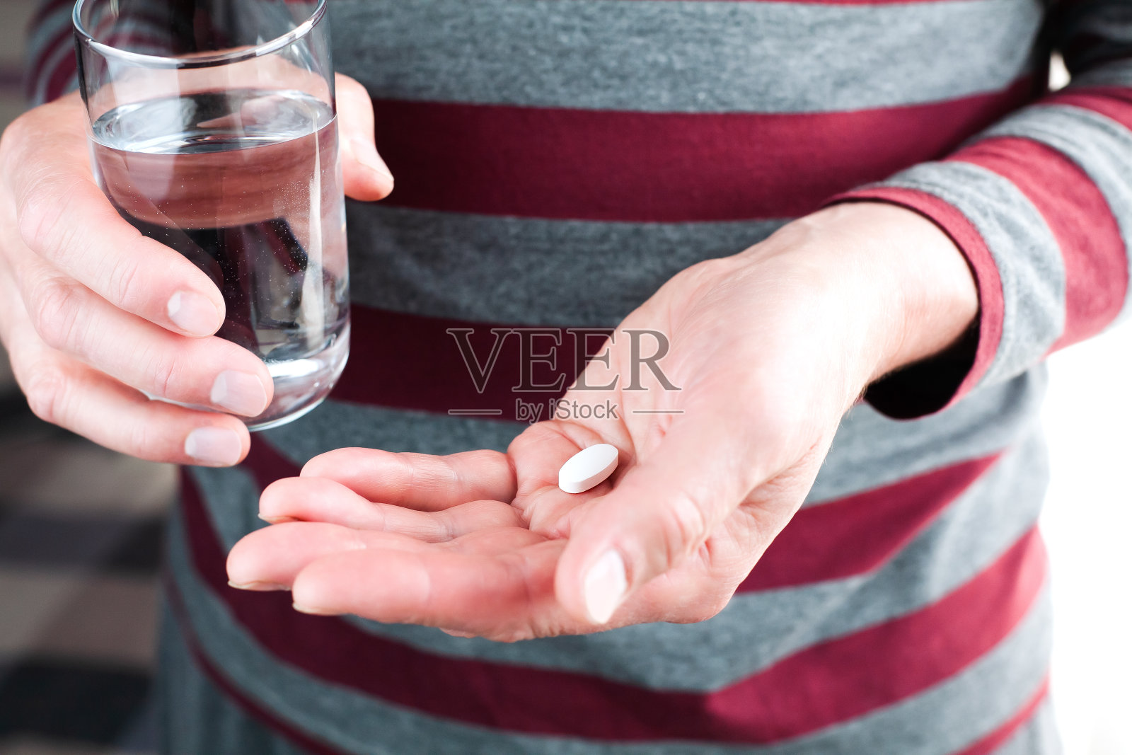 老人手里拿着一粒药和一杯水。遵医嘱服药。特写镜头。照片摄影图片