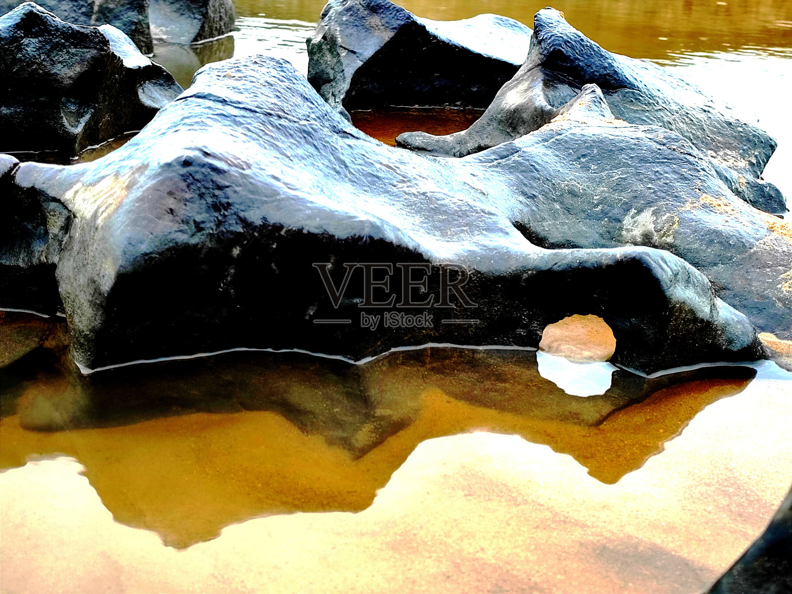 海滩上的一块石头，上面有一些洞，在一个岩池里。照片摄影图片