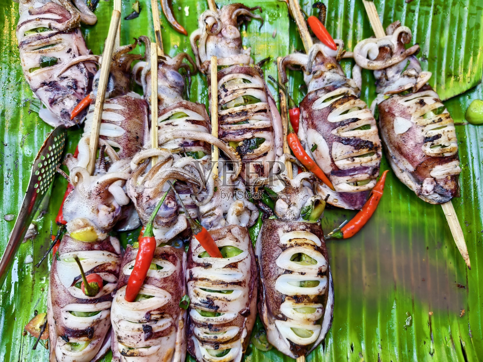 在一个充满活力的热带食品市场摊位上展示的烤墨鱼串和新鲜香草和香料的特写。照片摄影图片