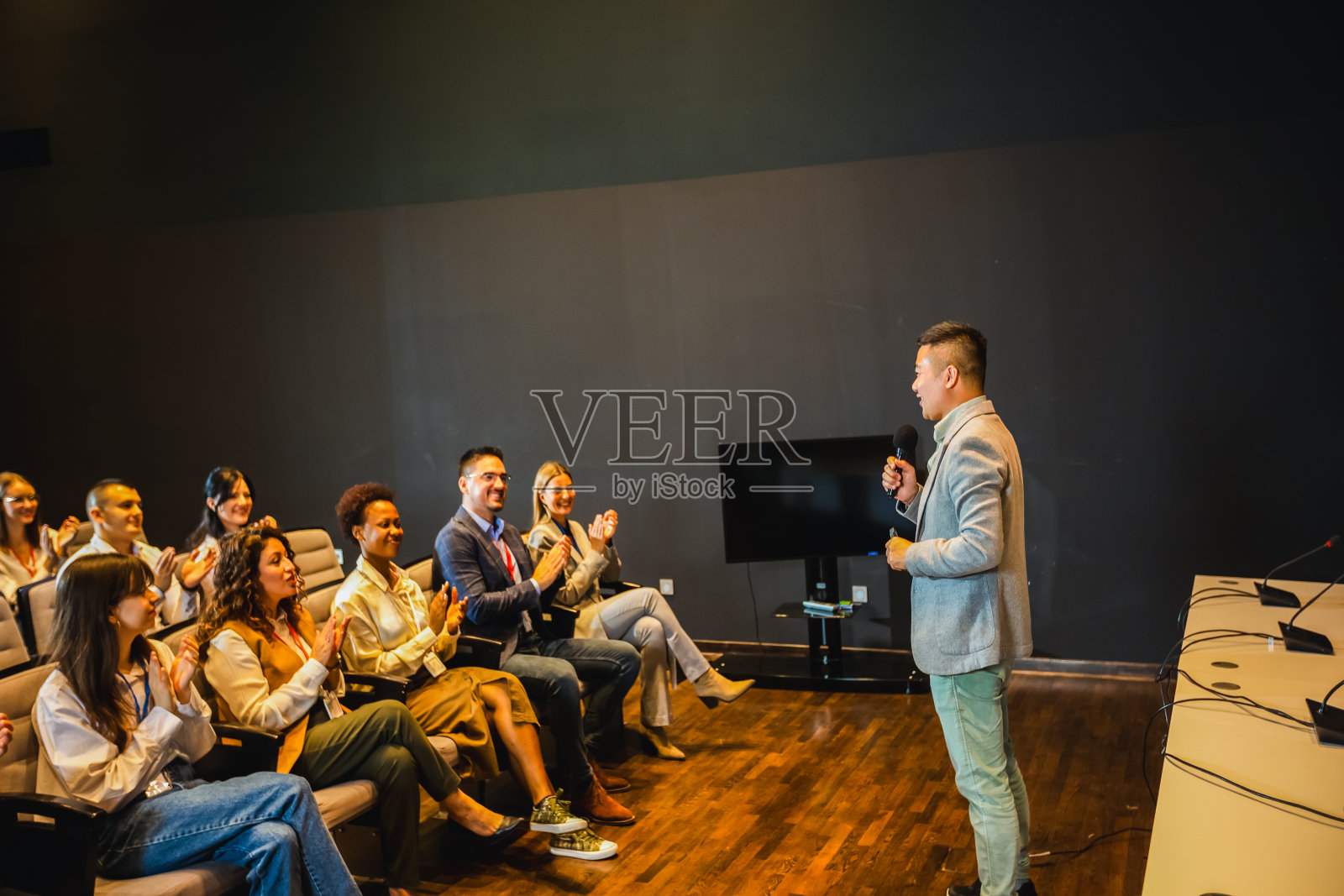 亚洲男性CEO在会议中心的新闻发布会上发表讲话。一群多种族的同事在倾听。照片摄影图片