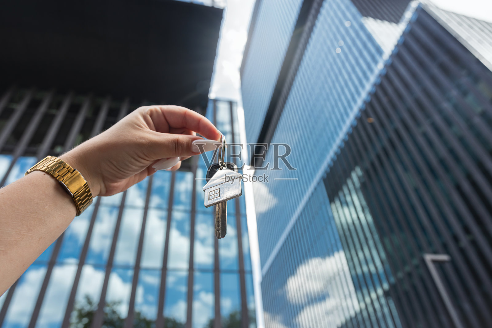 房地产经纪人拿着钥匙，背景是城市里的摩天大楼照片摄影图片