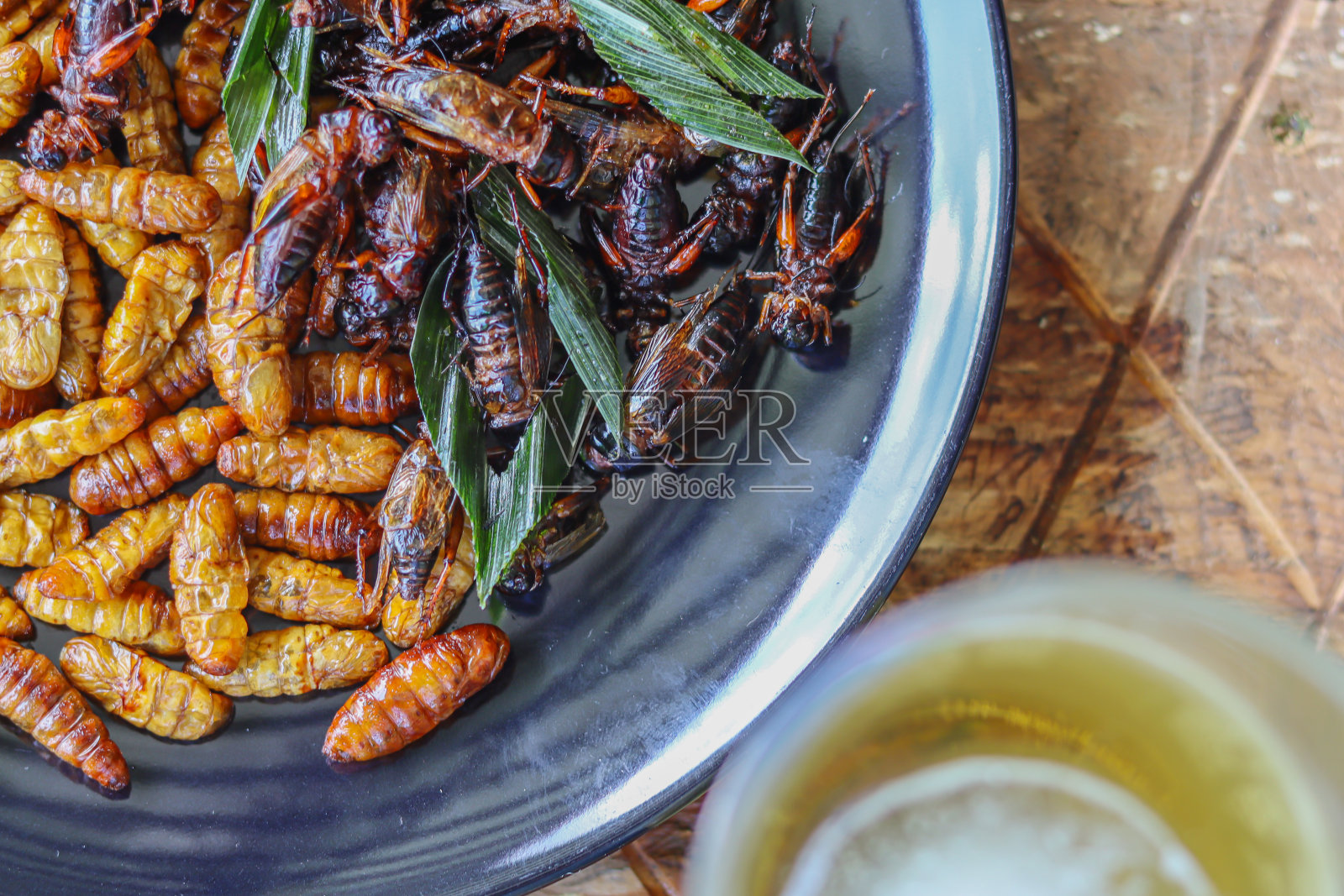 脆脆的昆虫装在黑色陶瓷盘子里，放在钢格栅做成的桌子上。炸昆虫是一种很受欢迎的食物，搭配酒精饮料，因为它们很容易找到，而且很受欢迎照片摄影图片