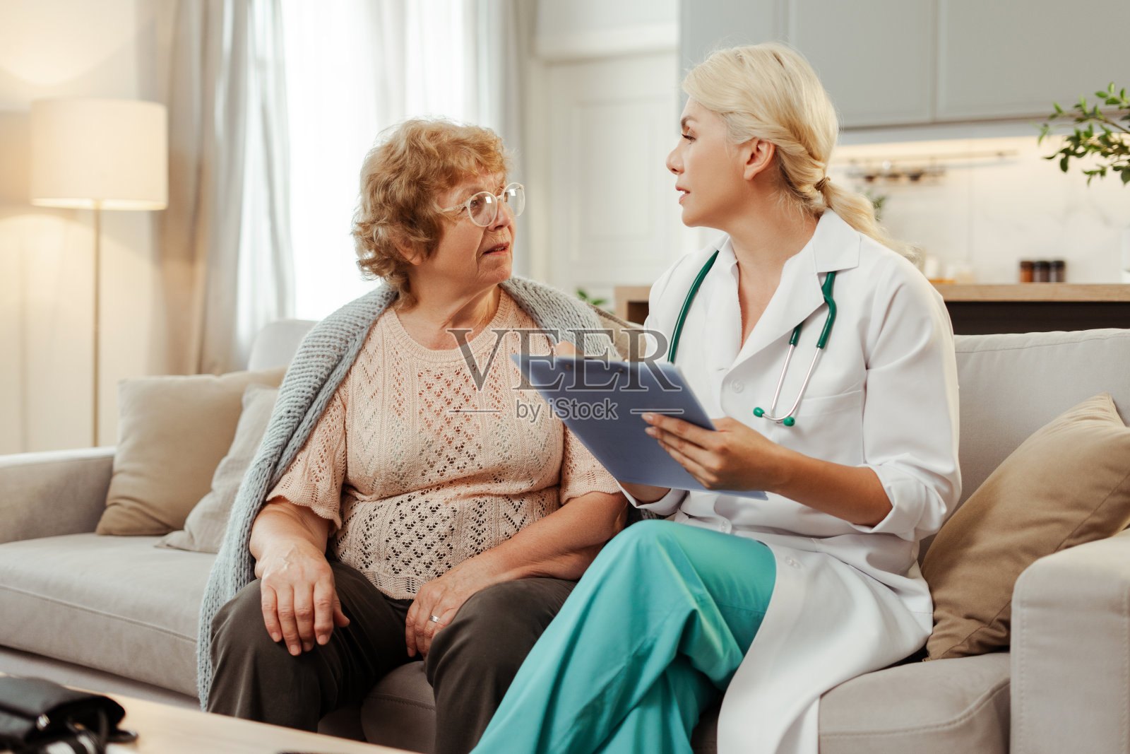 穿着白大褂的女医生拿着病历在家访中与老年病人交谈照片摄影图片