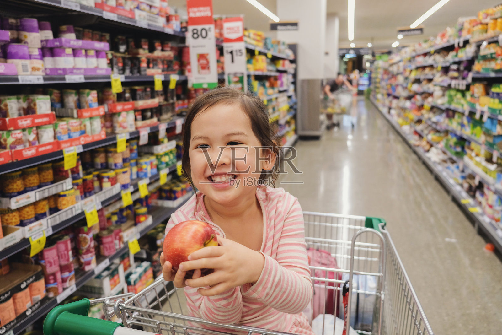 坐在商店的购物车里拿着苹果的快乐女孩照片摄影图片