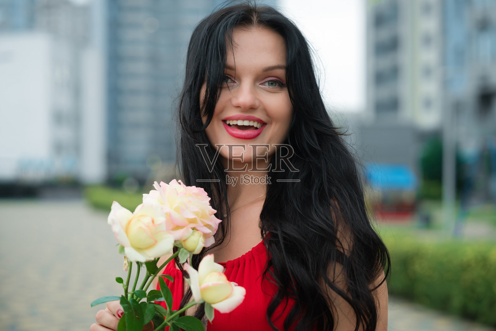 白天，在城市公园里，穿着红衣服的微笑女子手持一束玫瑰照片摄影图片