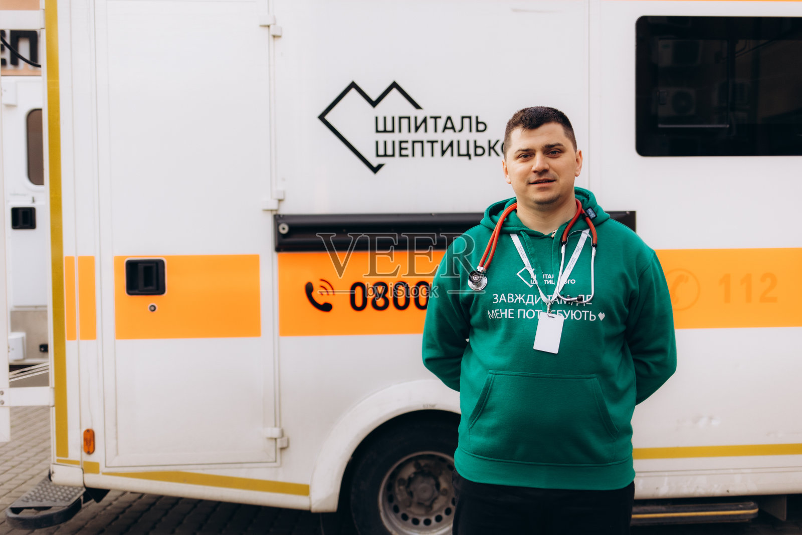 一个年轻的护理人员，站在一辆救护车的后面，站在敞开的车门旁边。他肩上扛着一个医疗创伤包，面带微笑，自信地看着镜头。照片摄影图片