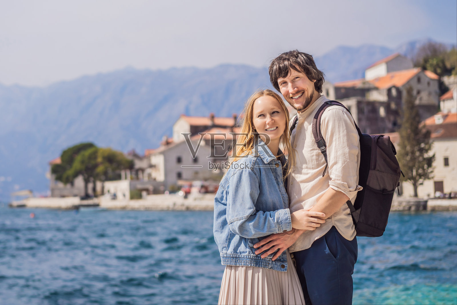 一对幸福的热恋男女游客在一个阳光明媚的日子里在黑山的佩拉斯特老城享受五彩缤纷的街道。黑山旅行的概念。在一个美丽的阳光明媚的日子里，著名的科托尔湾的历史小镇佩拉斯特的美景全景照片摄影图片