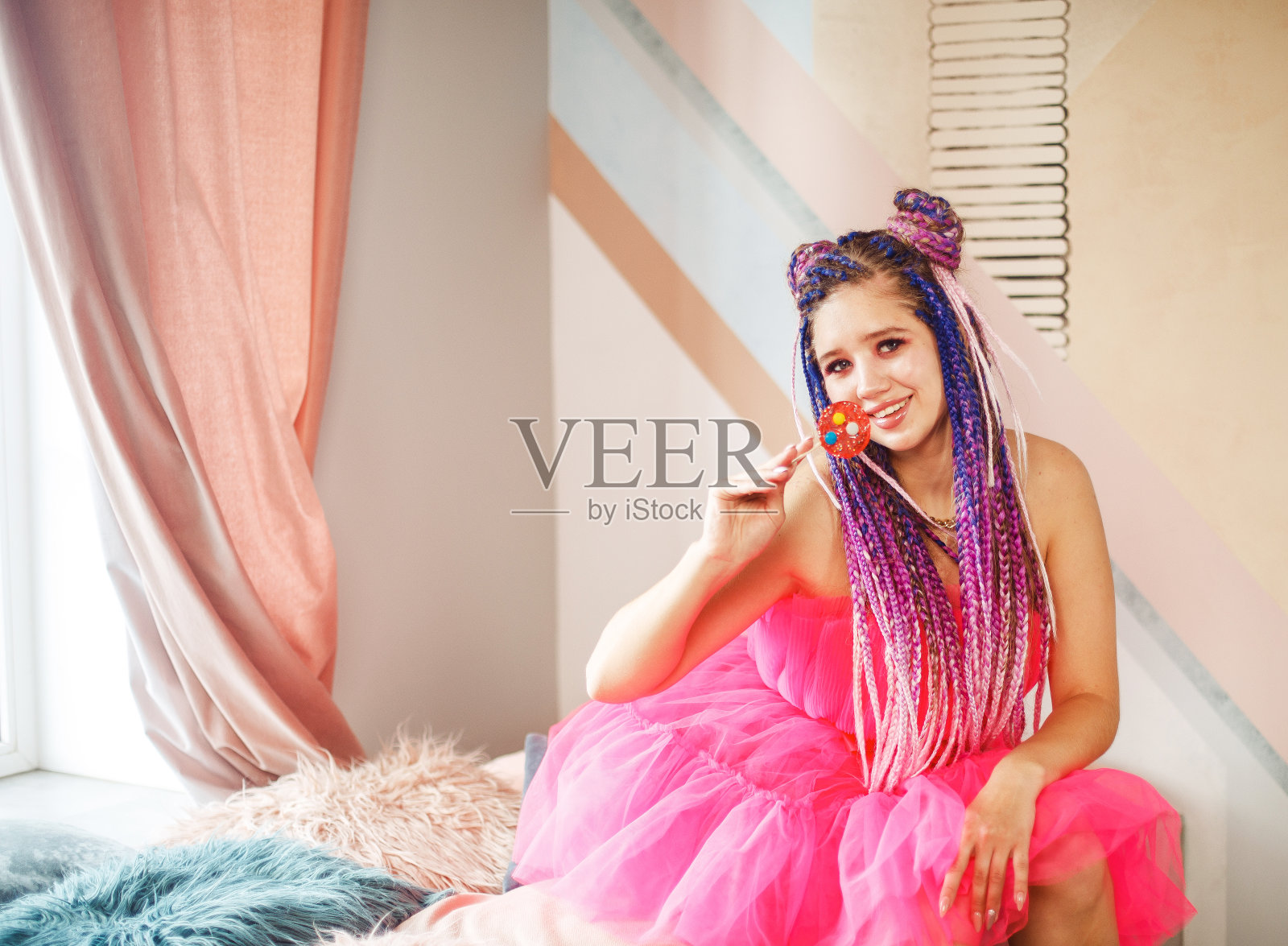 年轻女子留着脏辫发型，穿着粉红色的连衣裙，娃娃式的，明亮的妆容，在粉红色的房间里。照片摄影图片