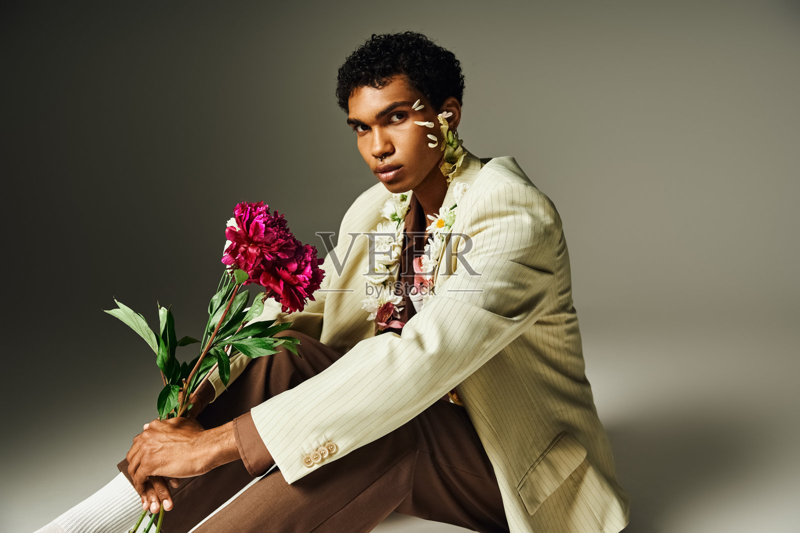 一个年轻的非裔美国人穿着一件时髦的运动上衣，脖子和脸上装饰着鲜花，在灰色的背景下摆姿势。照片摄影图片