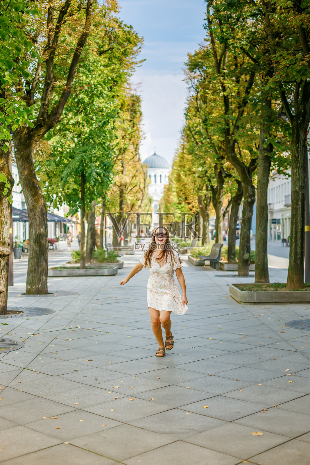 一个快乐的女人在绿树成荫的步行街上奔跑照片摄影图片