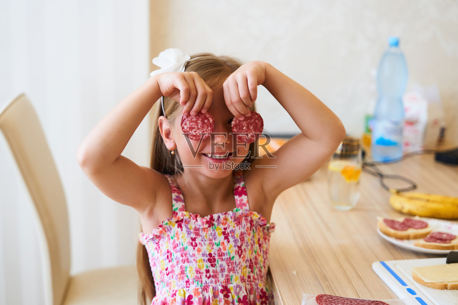 一个小女孩在明亮的厨房里微笑着玩着意大利腊肠片照片摄影图片