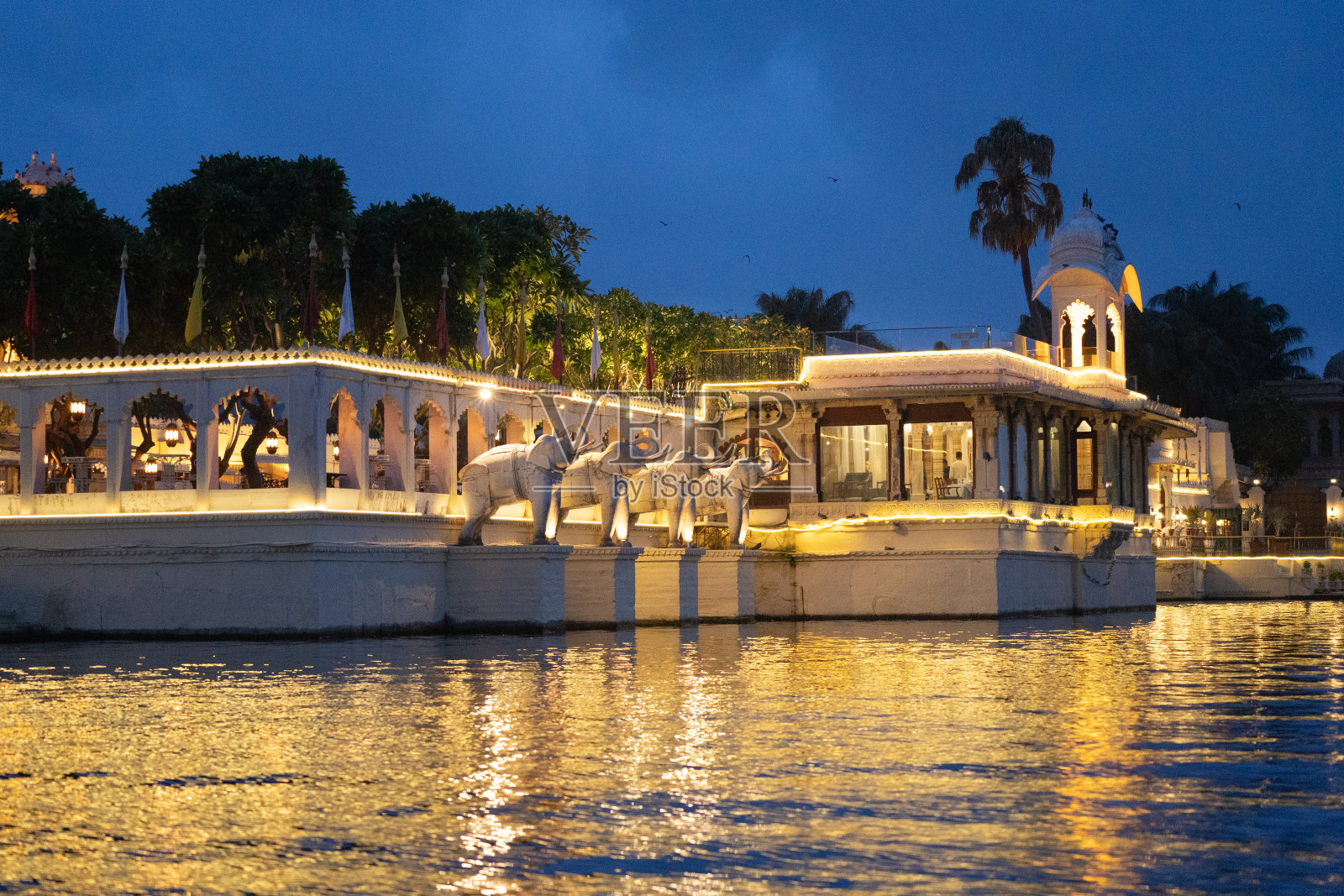 贾格曼迪尔岛宫殿，美丽的灯光反射在水中，有拱门，大象雕像和拱形窗户照片摄影图片