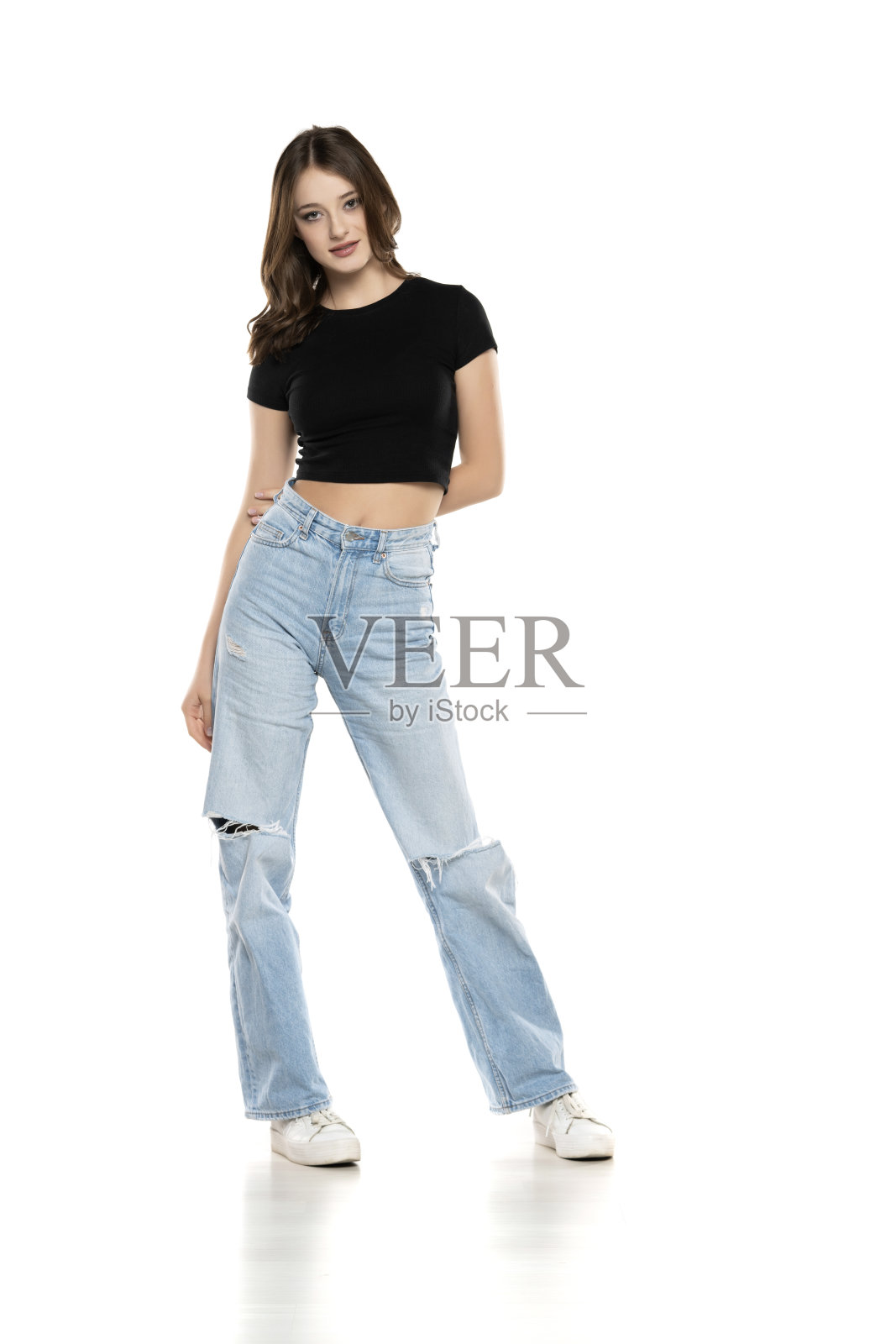 年轻的女模特穿着破洞牛仔裤和黑色衬衫在白色背景上摆姿势。前视图照片摄影图片