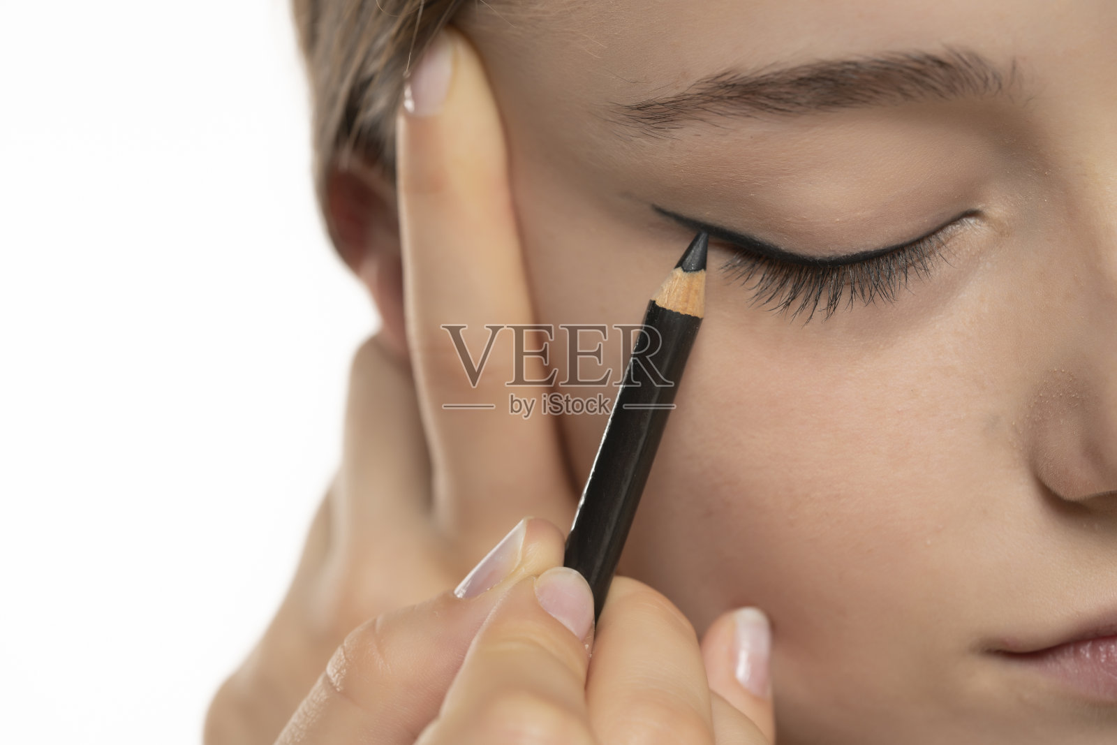 女子在白色背景上用铅笔在眼睑上画眼线照片摄影图片