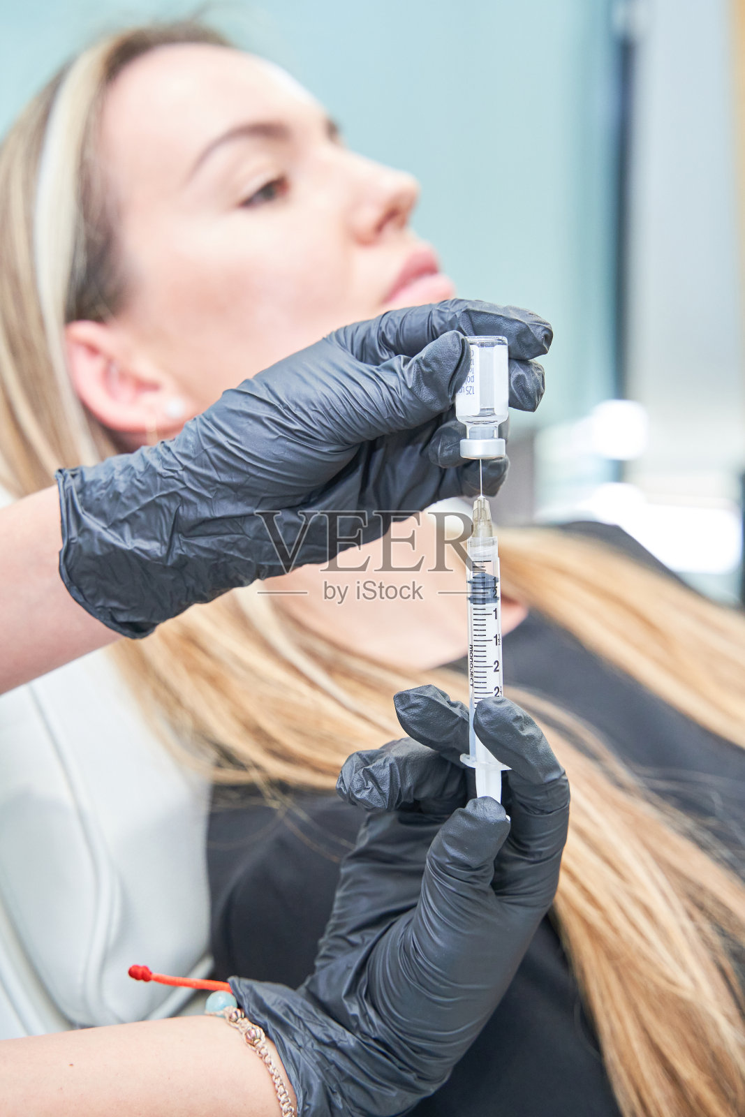 一个女人拿着注射器。注射器是白色的，女人戴着黑色的手套。照片摄影图片