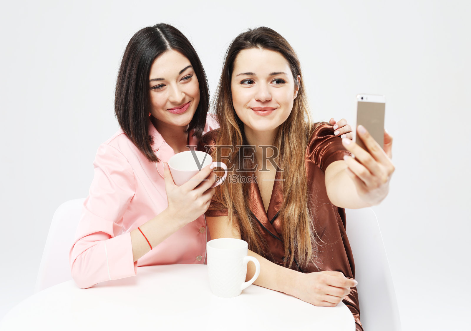 两个穿着睡衣的快乐女性朋友喝着咖啡，自拍。照片摄影图片