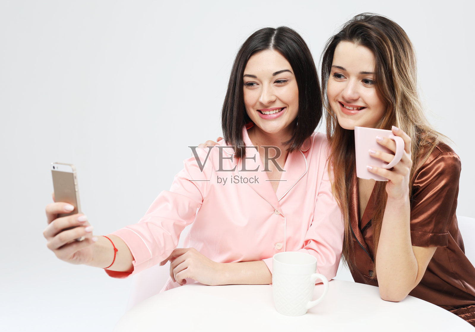 两个穿着睡衣的快乐女性朋友喝着咖啡，自拍。照片摄影图片