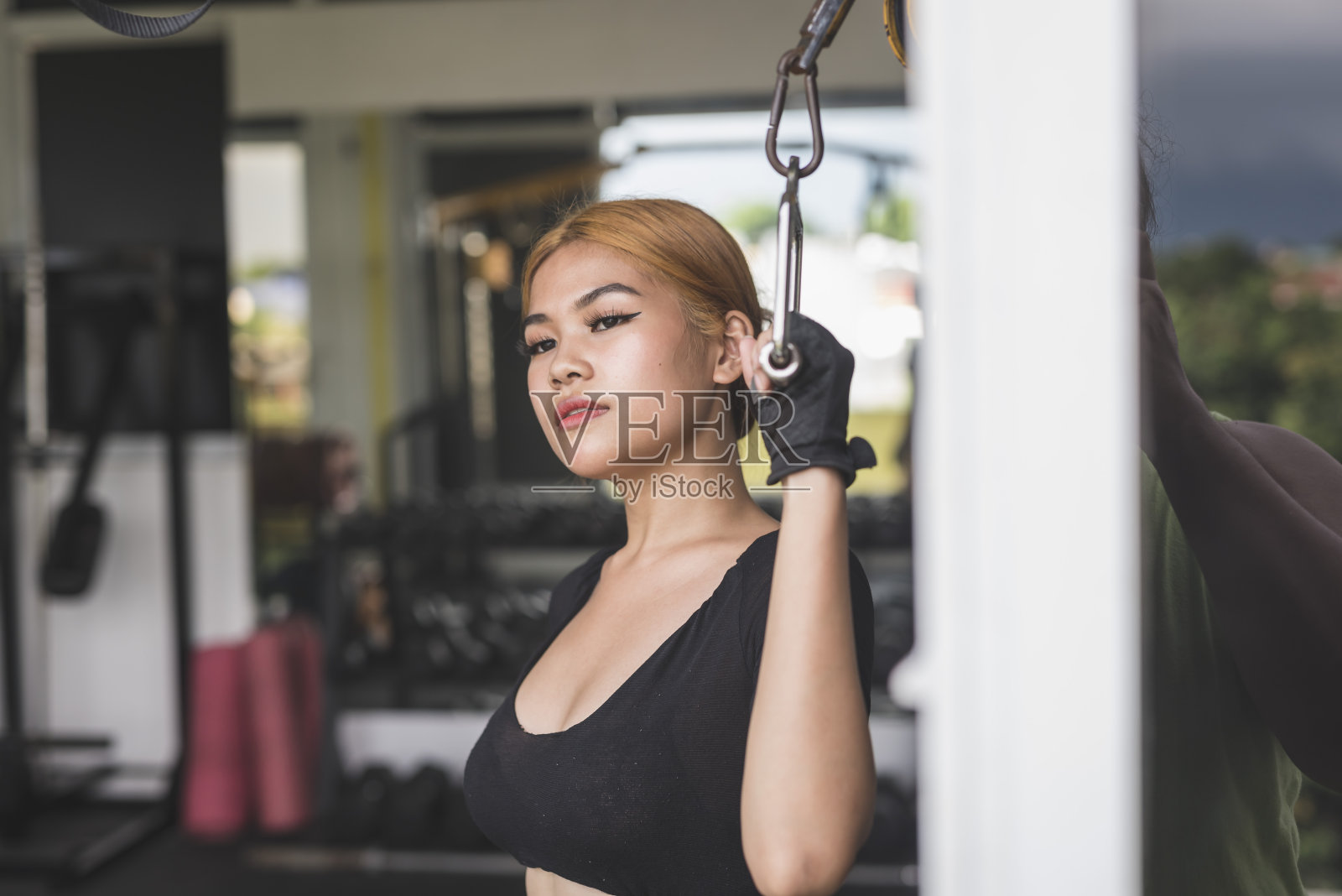 一位年轻的亚洲女子抓着钢索把手沉思。在健身房沉思的时候。照片摄影图片
