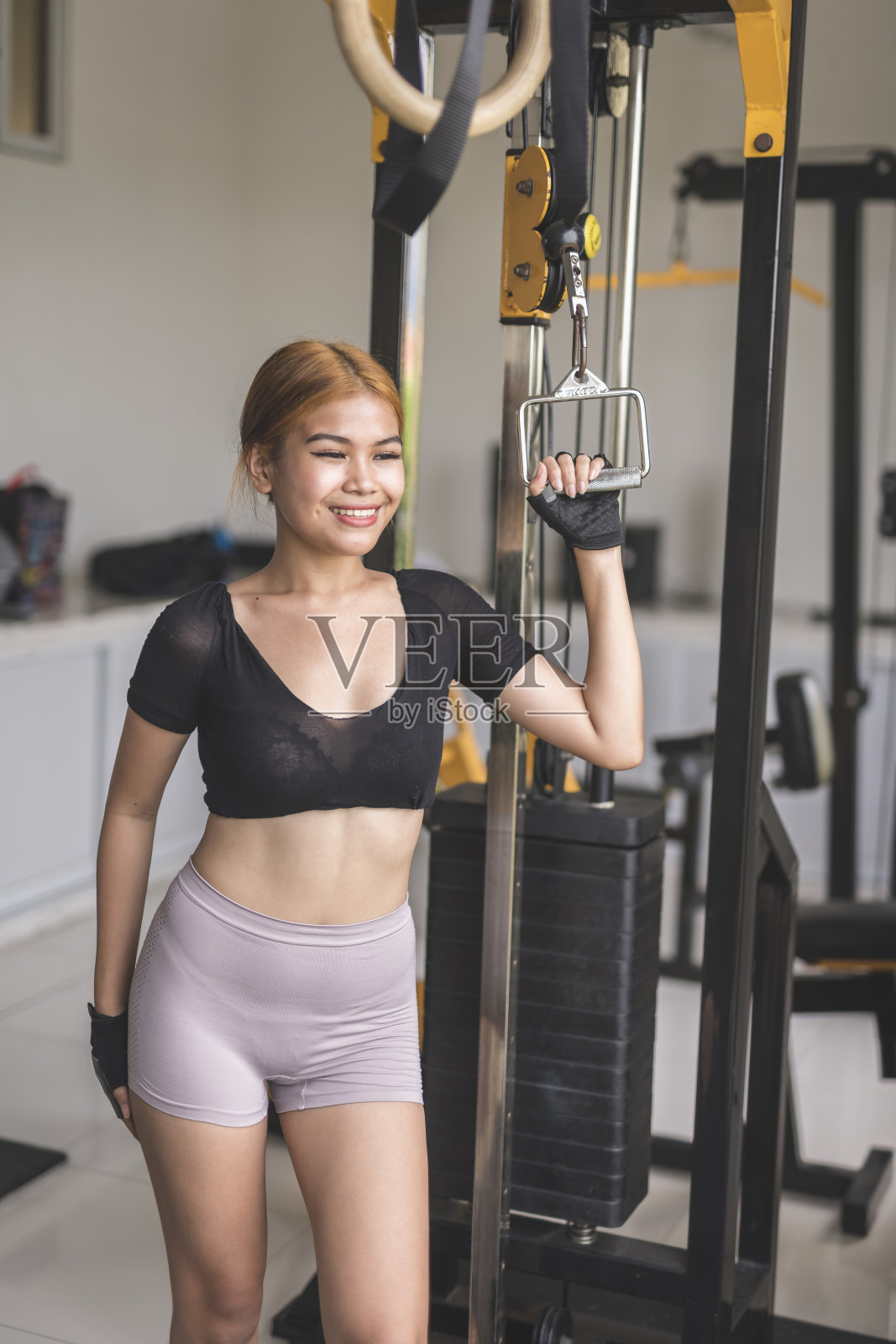 一位乐观的年轻女子微笑着抓着酒吧的钢索把手。在健身房的时候想着快乐的事情。照片摄影图片