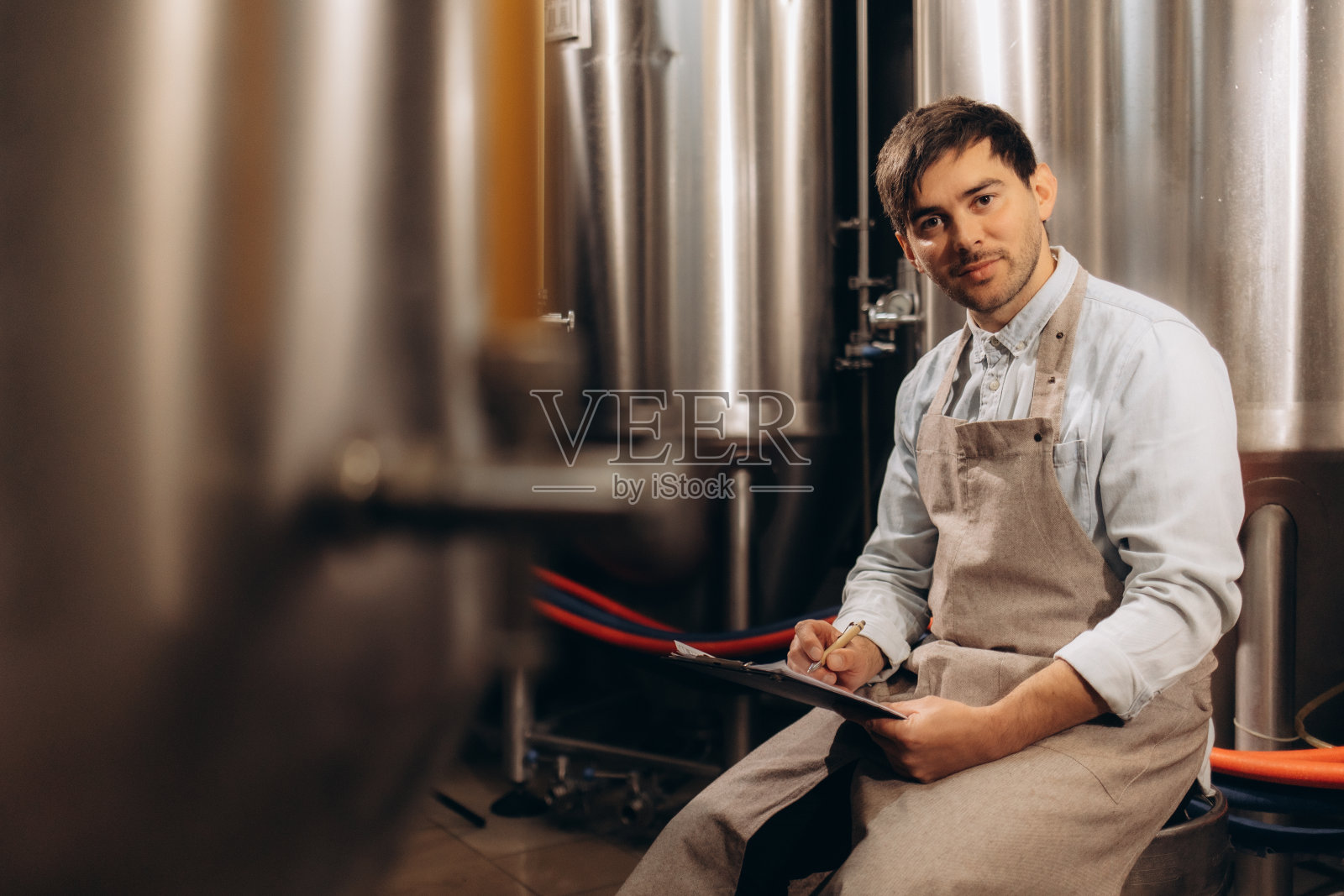 一位留着胡子的年轻酿酒师在酿造过程中监控着传感器的读数。使啤酒。照片摄影图片