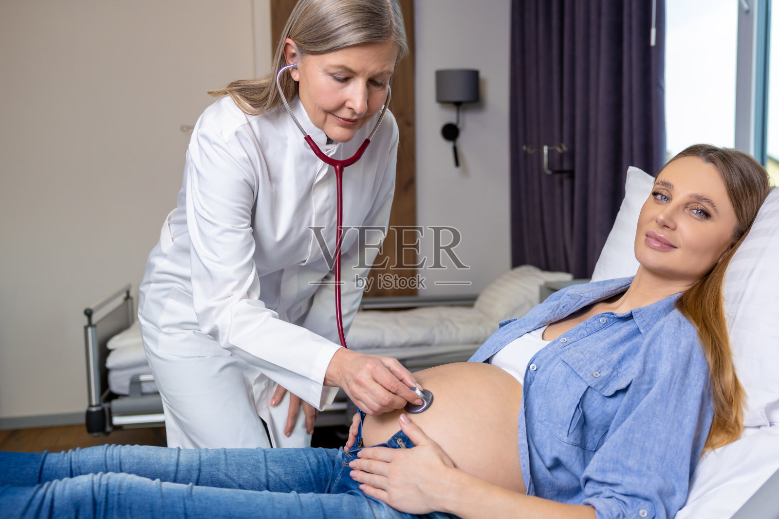 孕妇躺在沙发上，医生在听婴儿的心跳照片摄影图片