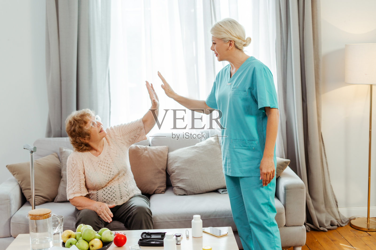 护士在家里的沙发上和快乐的老女人击掌照片摄影图片