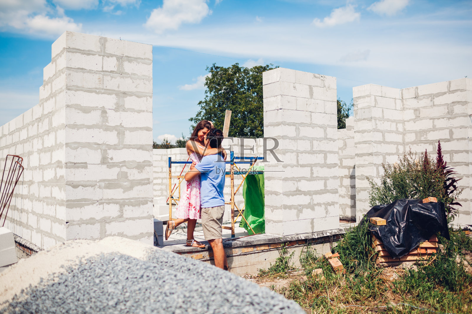 幸福的年轻夫妇在他们未来正在建设的房子前拥抱。男人和女人想象他们的家照片摄影图片