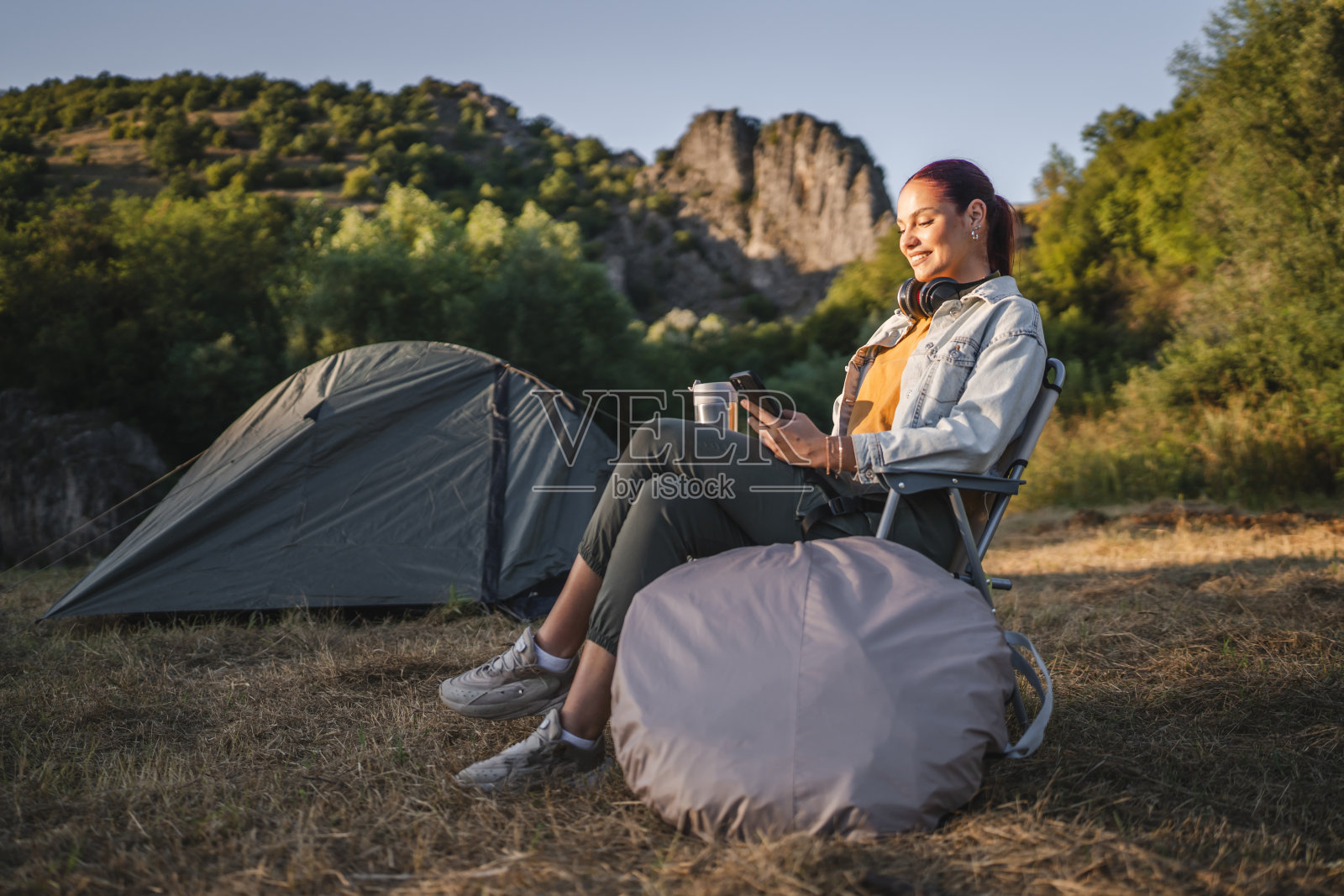 年轻女子坐在帐篷前，用手机和喝咖啡照片摄影图片