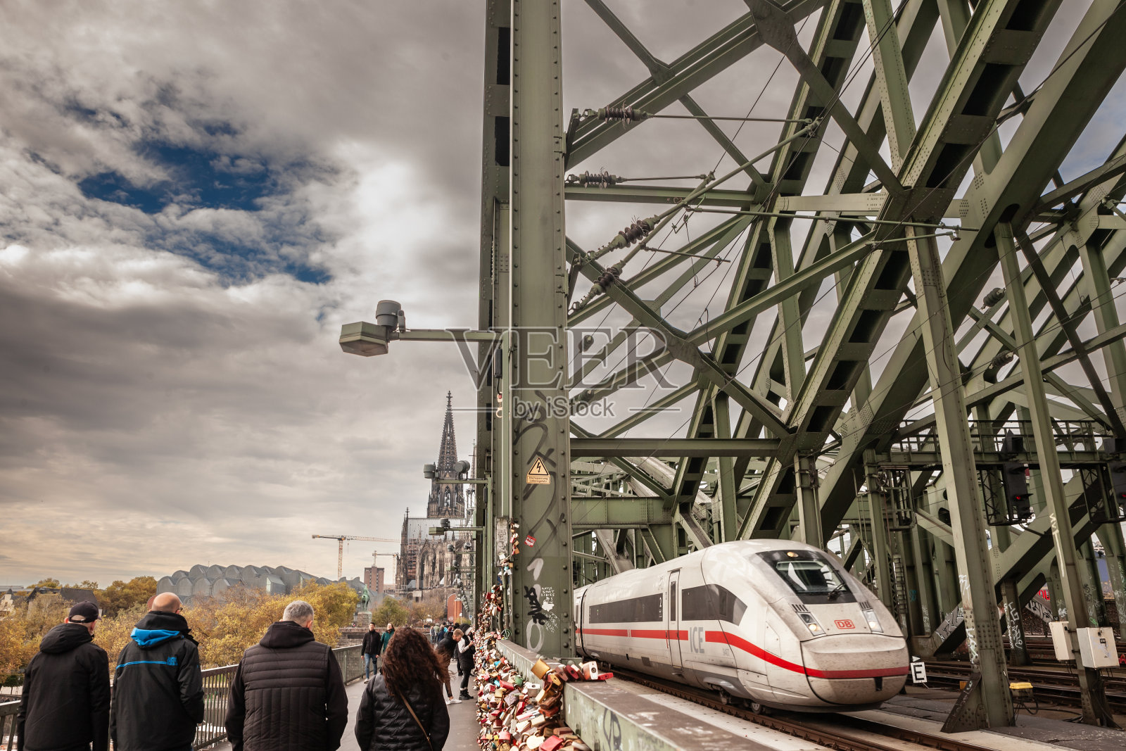 德国科隆,一列DB高速ICE列车经过霍亨索伦大桥,旁边是行人。霍亨索伦桥是一座铁路桥。照片摄影图片