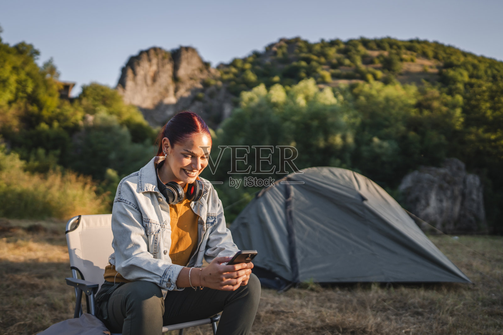 戴着耳机的年轻女子坐在帐篷前使用手机照片摄影图片