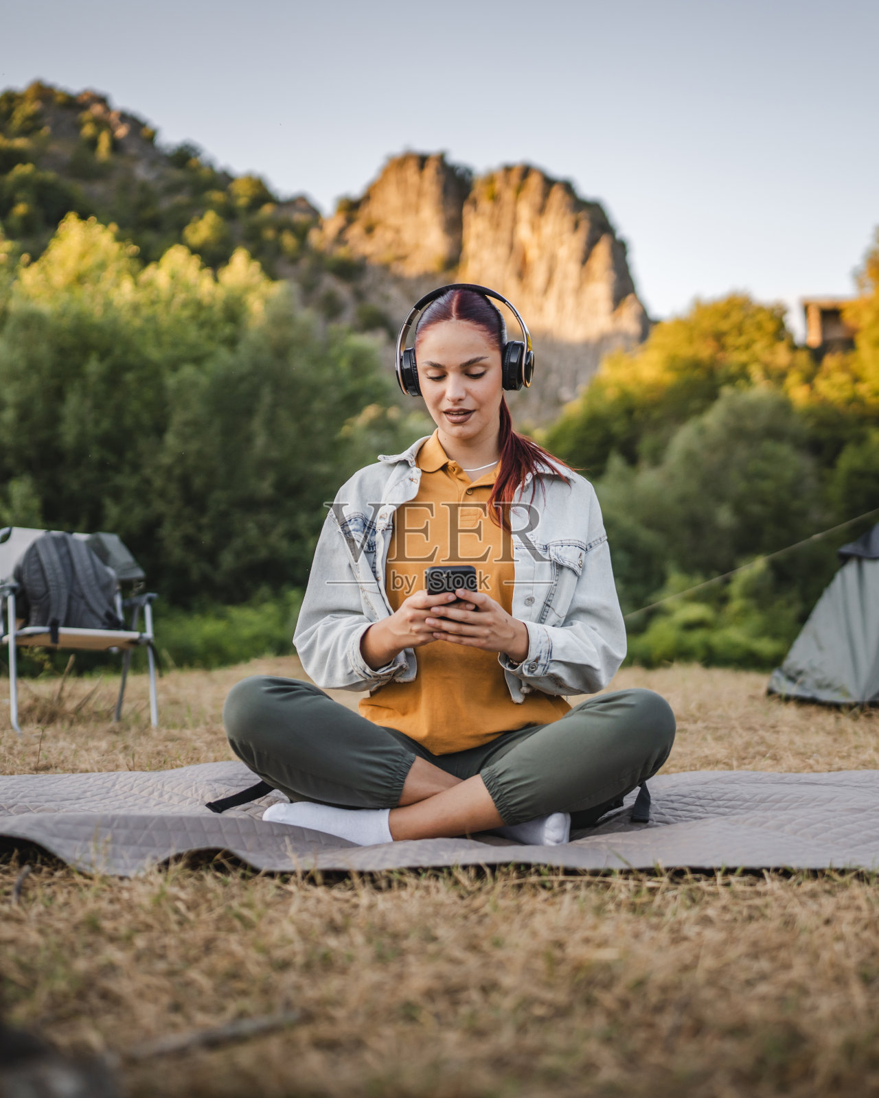 年轻女子戴着耳机听音乐，坐在毯子上照片摄影图片