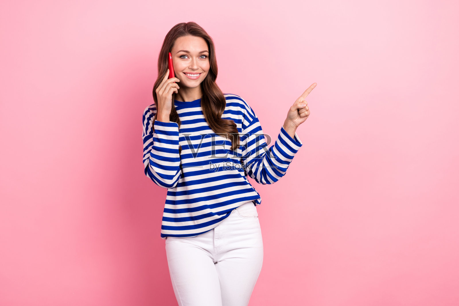 有趣可爱的女孩的肖像，卷发，条纹衣服，讲电话，指导空白空间，孤立在粉红色的背景照片摄影图片
