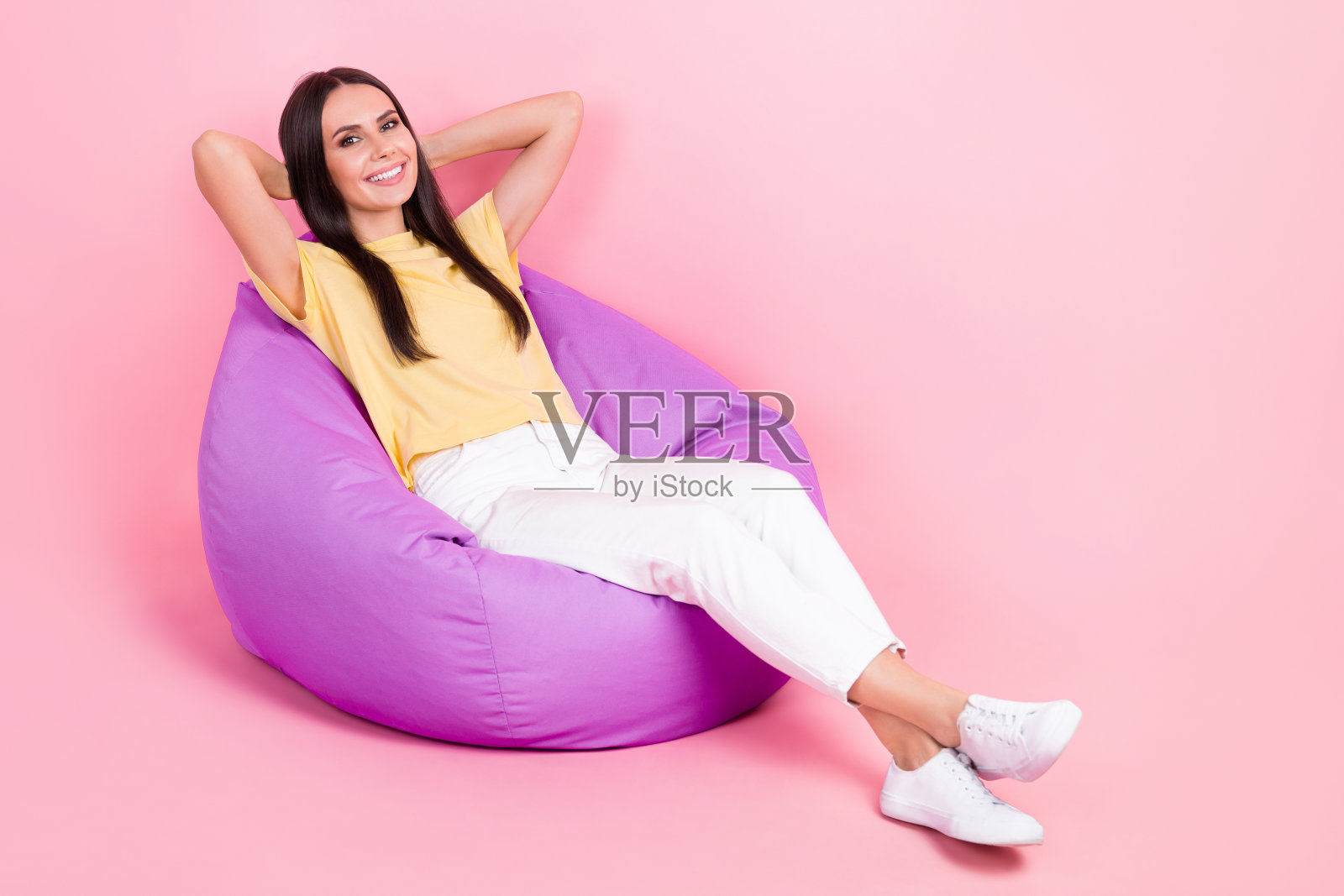 漂亮甜美的女士穿着黄色t恤的全身照片，坐在豆袋手臂后面的头空的空间孤立的粉红色背景照片摄影图片