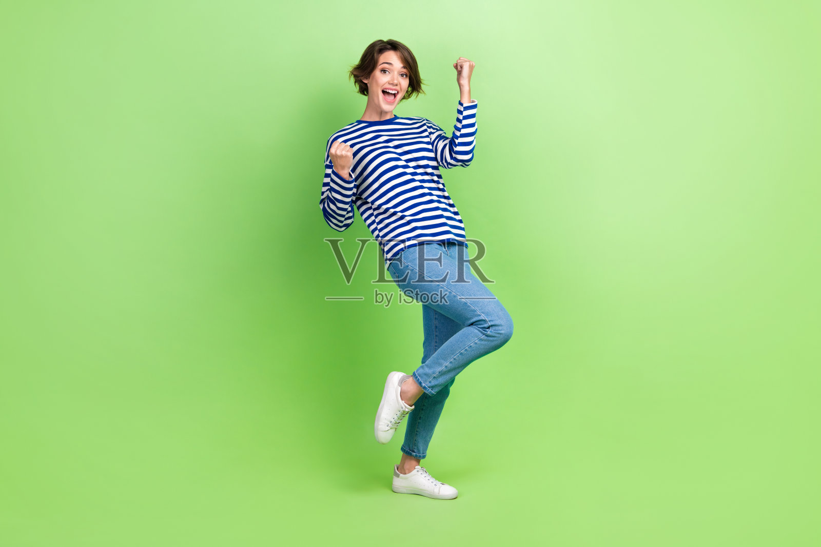 穿着条纹运动衫的女孩在绿色背景下举起拳头赢得赌博照片摄影图片