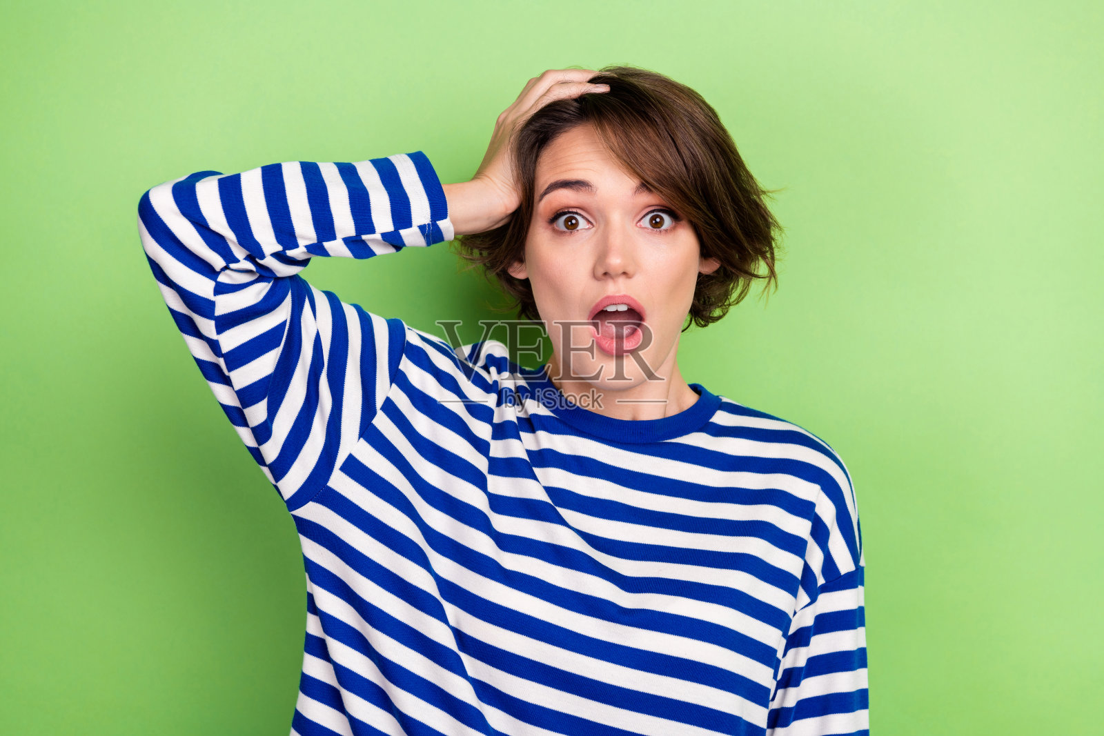 可爱的印象女孩短发穿着水手长袖凝视手臂在头部孤立的绿色背景照片摄影图片