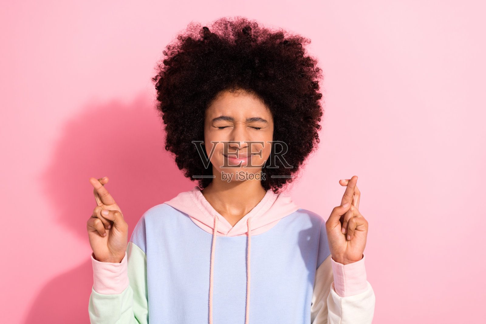 照片紧张的小学生闭上眼睛，交叉手指，期待祈祷运气，想要等待孤立在粉红色的背景照片摄影图片