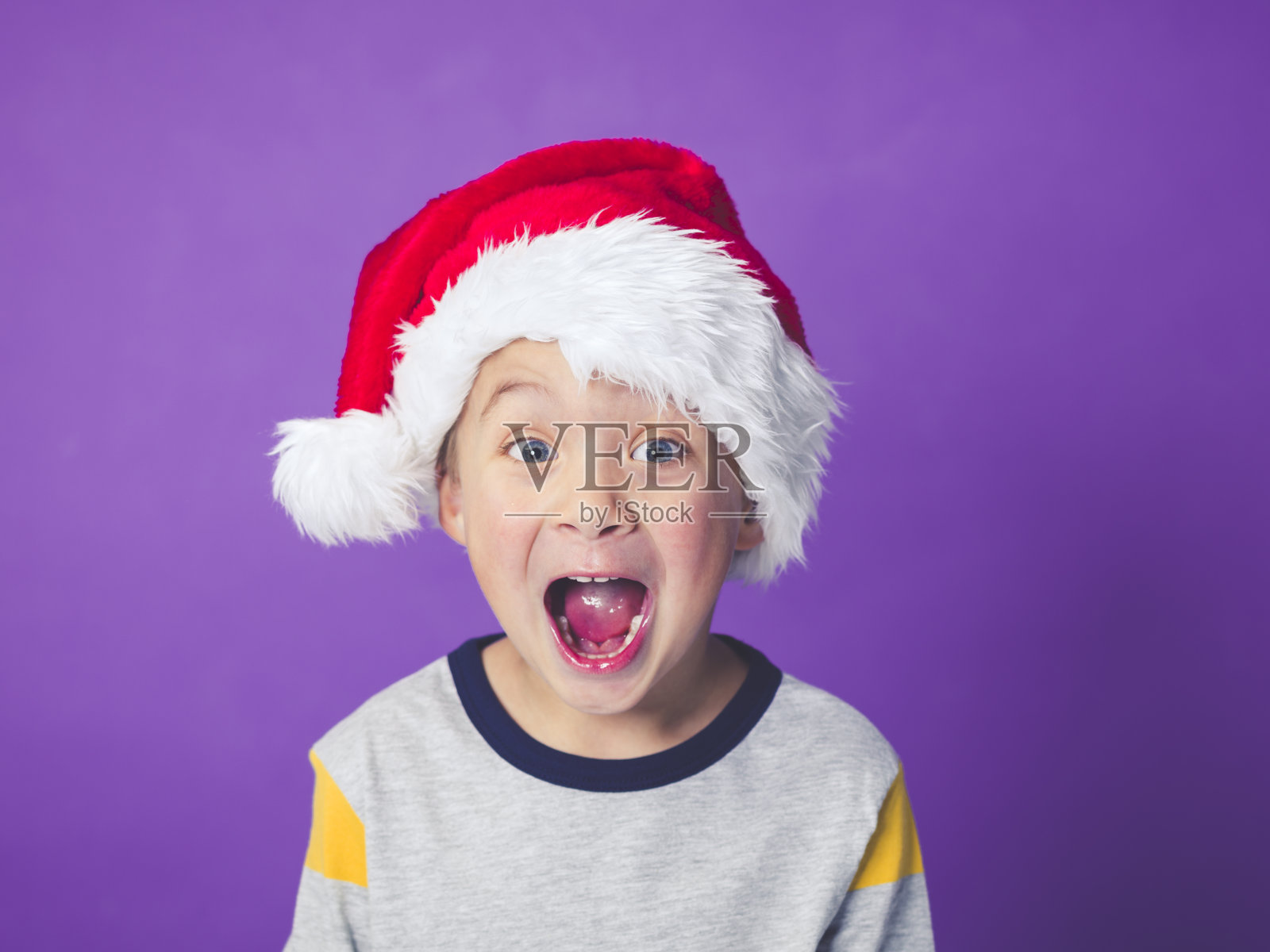 紫色背景下戴圣诞帽的男孩照片摄影图片