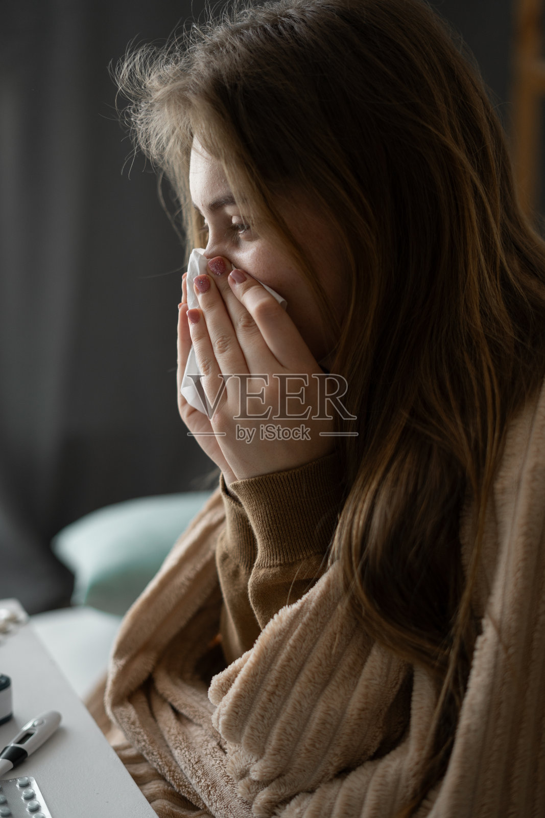 在家请病假。有流鼻涕和普通感冒的女人。她打了个喷嚏，擦了擦鼻子。患感冒或流感的。一个不健康的女孩的肖像。照片摄影图片