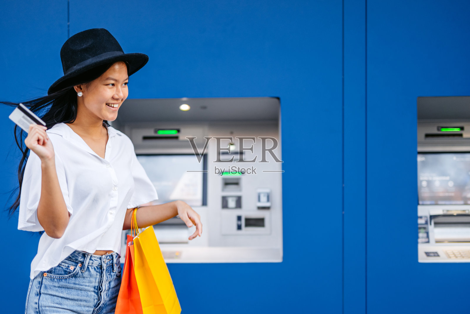 在西班牙巴塞罗那，一名年轻的亚洲女子拎着购物袋在自动取款机前用信用卡取钱照片摄影图片