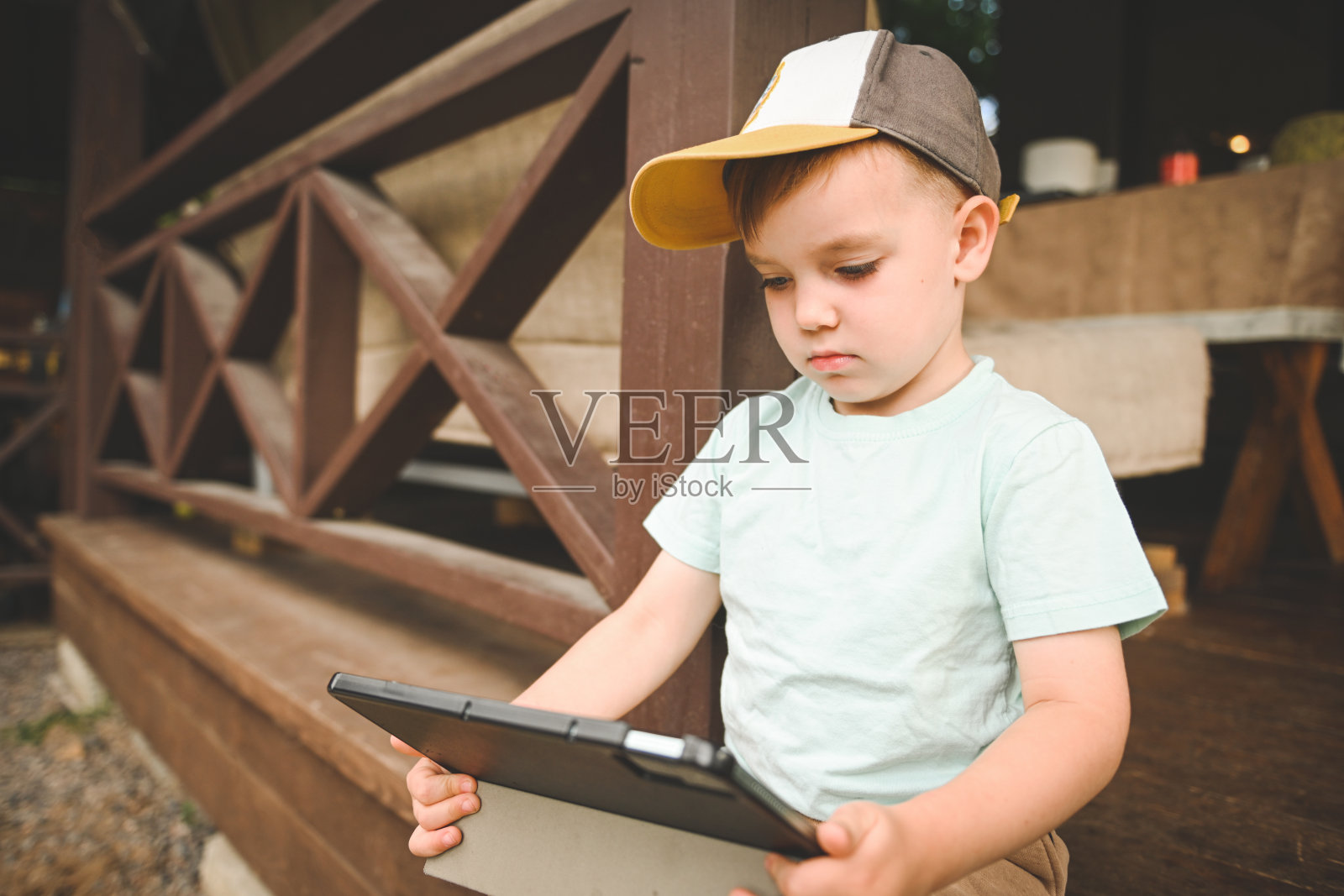 坐在房屋门廊上玩平板电脑的可爱小男孩照片摄影图片