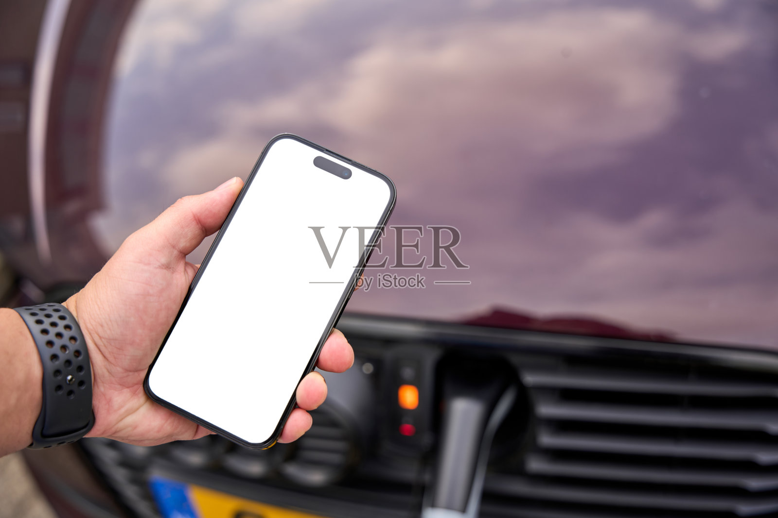 这个年轻人给他的电动汽车充电，并通过手机控制它。照片摄影图片