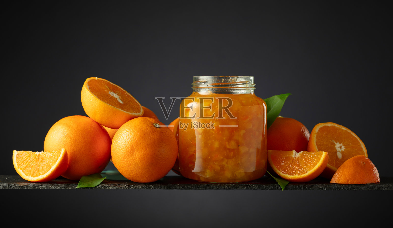 玻璃罐里的橘子酱和黑色背景上的新鲜水果。照片摄影图片
