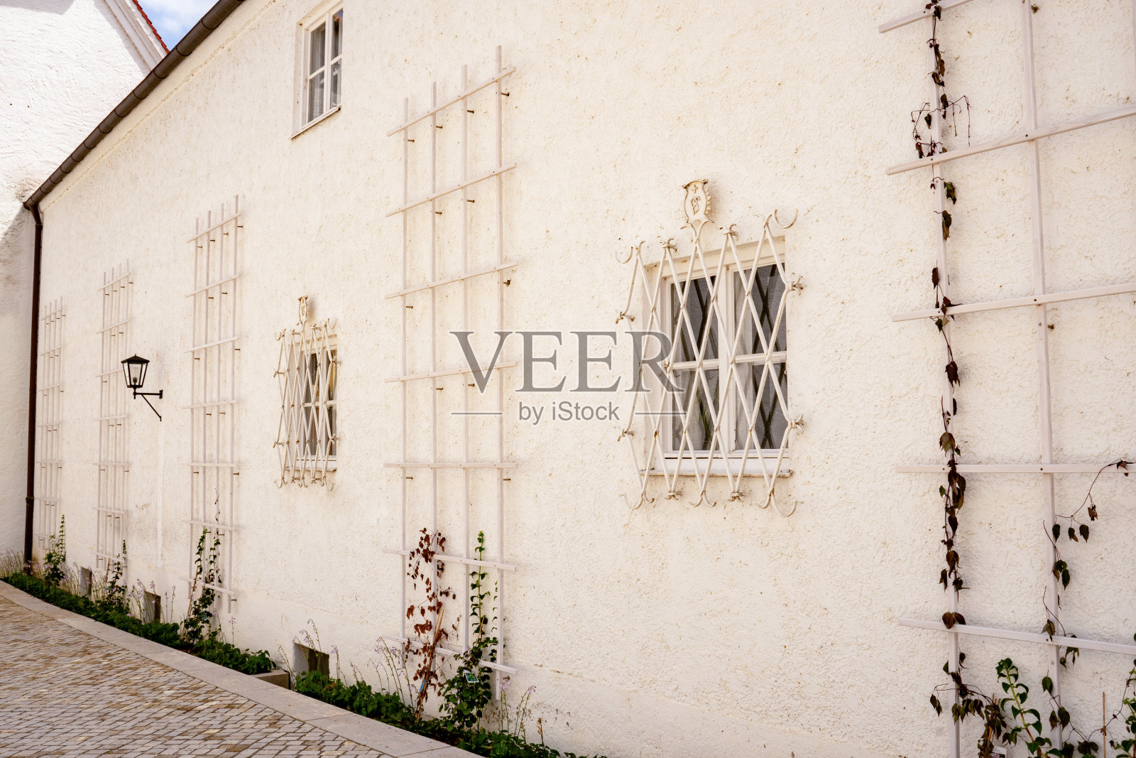 德国巴伐利亚州弗赖辛的圣玛丽亚和科尔比尼大教堂旁边的白色墙壁，窗户上装有白色的窗棂和白色的格子架，供攀缘植物使用照片摄影图片