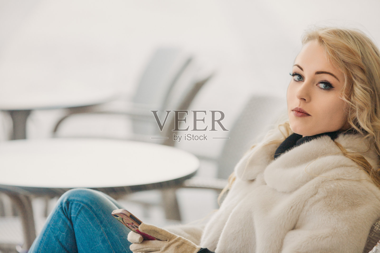 漂亮的年轻女子穿着白色皮大衣坐在咖啡馆里照片摄影图片