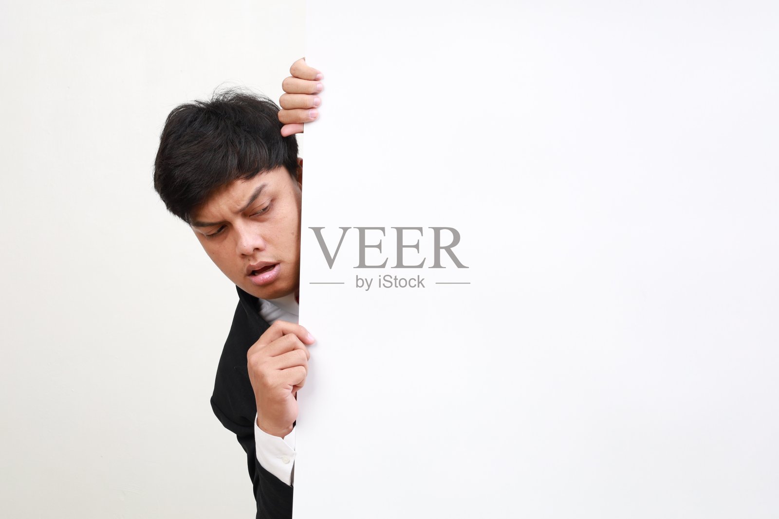 好奇的穿着正装的亚洲商人从模型墙后面偷看。照片摄影图片