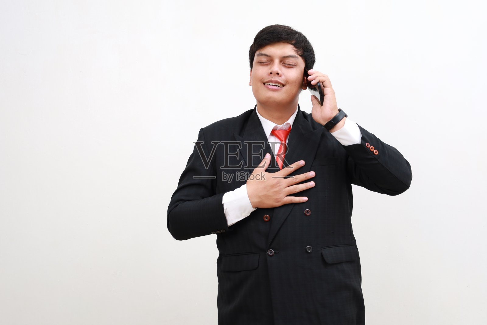 站在电话旁的印尼商人员工如释重负，心情愉快。孤立于白色照片摄影图片